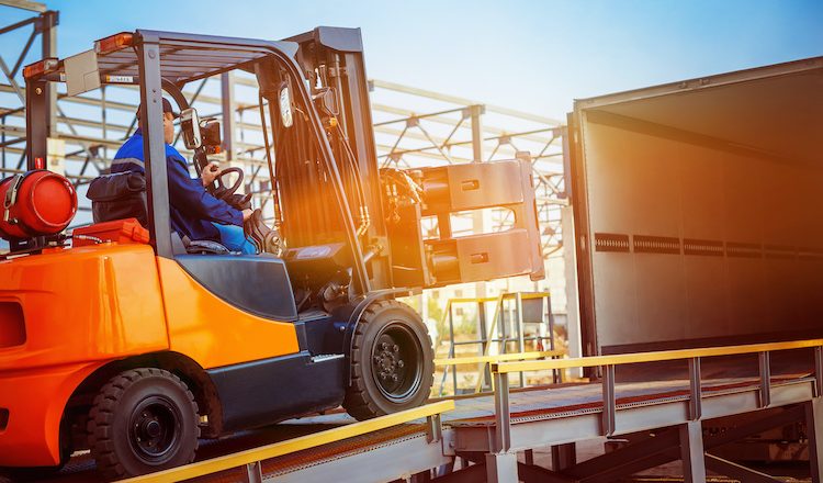 Forklift is putting cargo from warehouse to truck outdoors